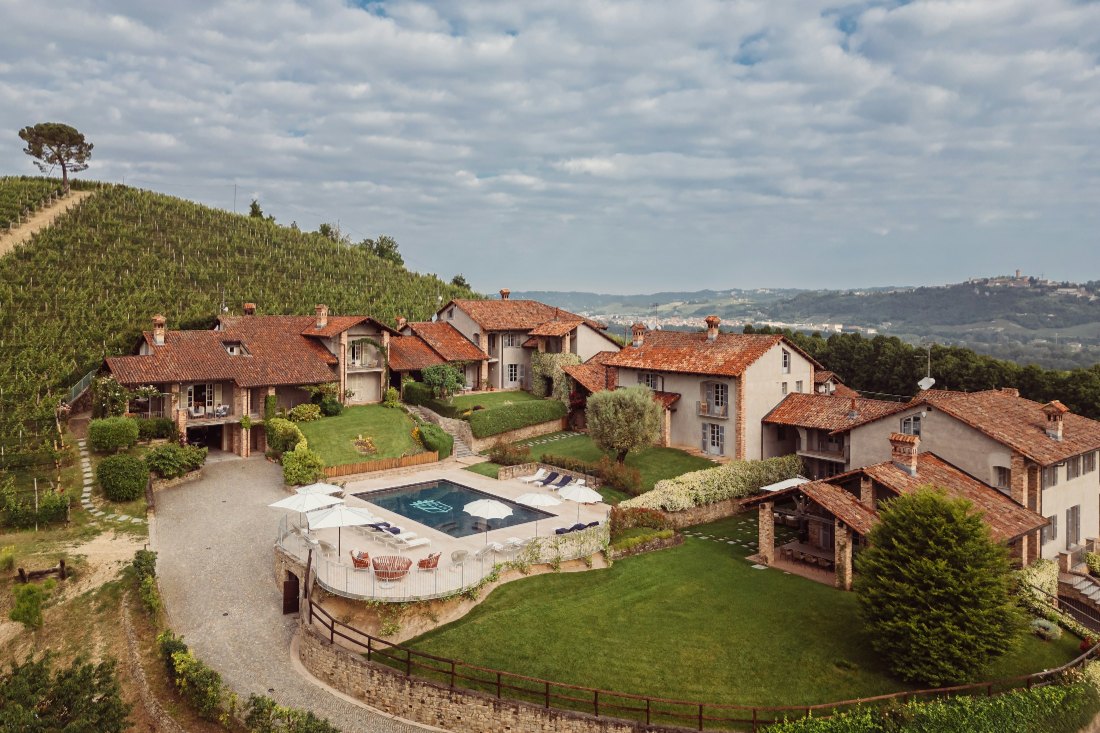 A country estate of tiled roofs around a pool, with vineyards on the hillside behind